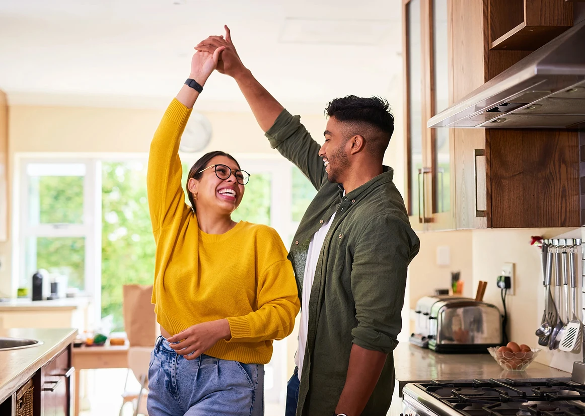 Smiling couple dancing joyfully together in a bright kitchen.